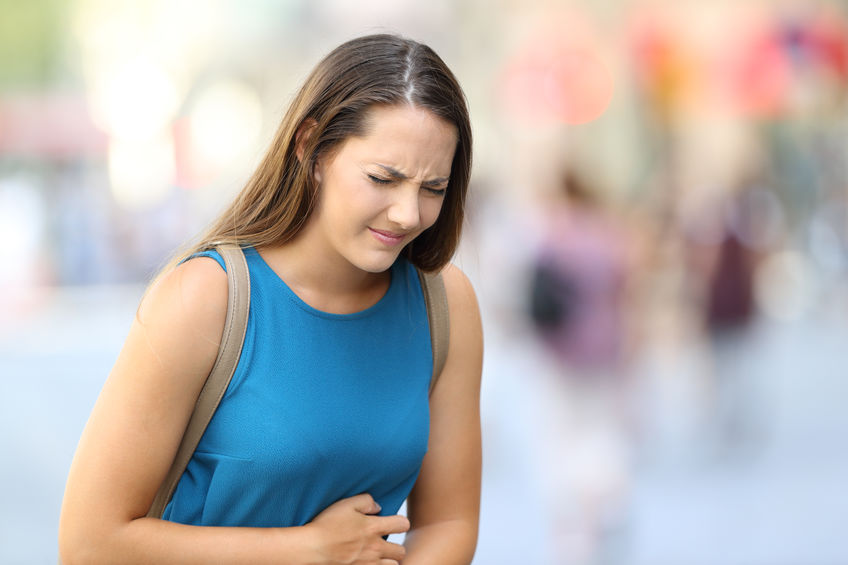 Mulher na rua sente cólicas e coloca a mão sobre a barriga.