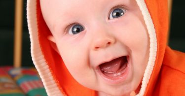 Bebê branco. sem dentes, sorrindo com a boca aberta, embrulhado em uma roupa laranja.