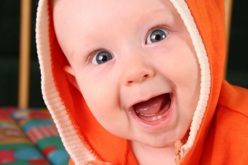 Bebê branco. sem dentes, sorrindo com a boca aberta, embrulhado em uma roupa laranja.