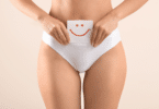 Mulher segurando papel com rosto feliz desenhado, perto da barriga