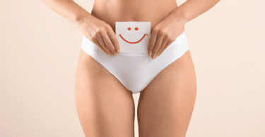 Mulher segurando papel com rosto feliz desenhado, perto da barriga