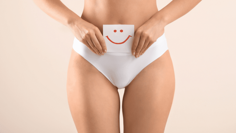 Mulher segurando papel com rosto feliz desenhado, perto da barriga