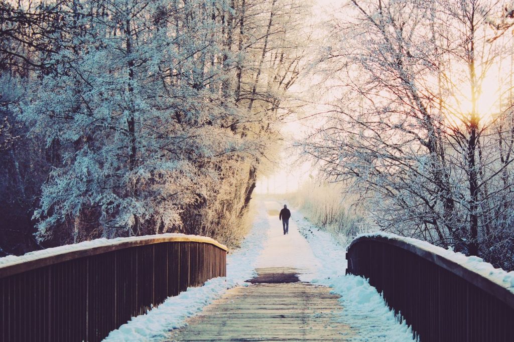 Homem visto de costas após atravessar uma ponte em paisagem de inverno.