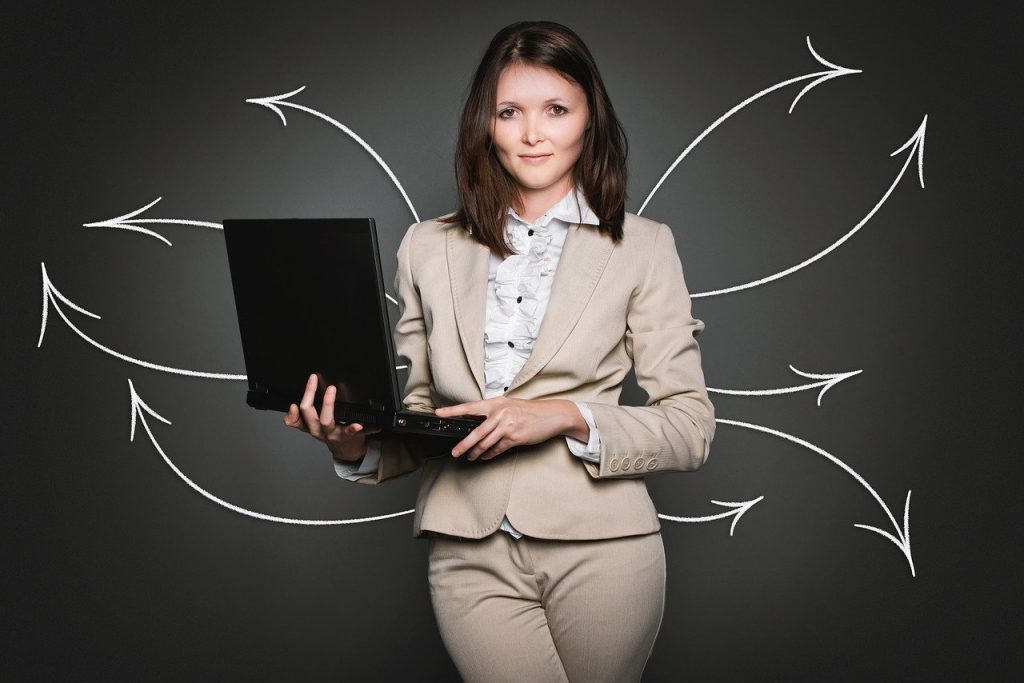 Mulher com roupas sociais segurando um notebook. Ao fundo, setas brancas partem de trás da mulher e saem em diferentes direções.