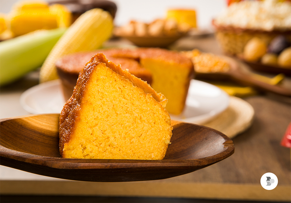 Dois pedaços de bolo de milho. Um pedaço está sendo servido em um prato de madeira pequeno e redondo e o outro pedaço servido em um prato de porcelana pequeno e redondo.
