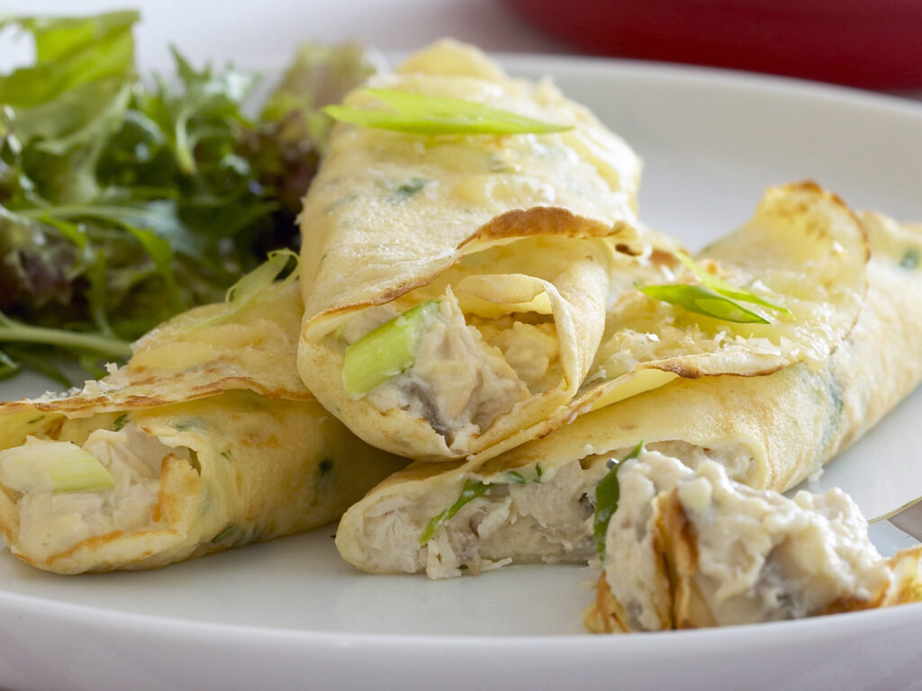 Três crepiocas prontas para serem servidas. Estão sobre um prato branco e de acompanhamento salada verde.
