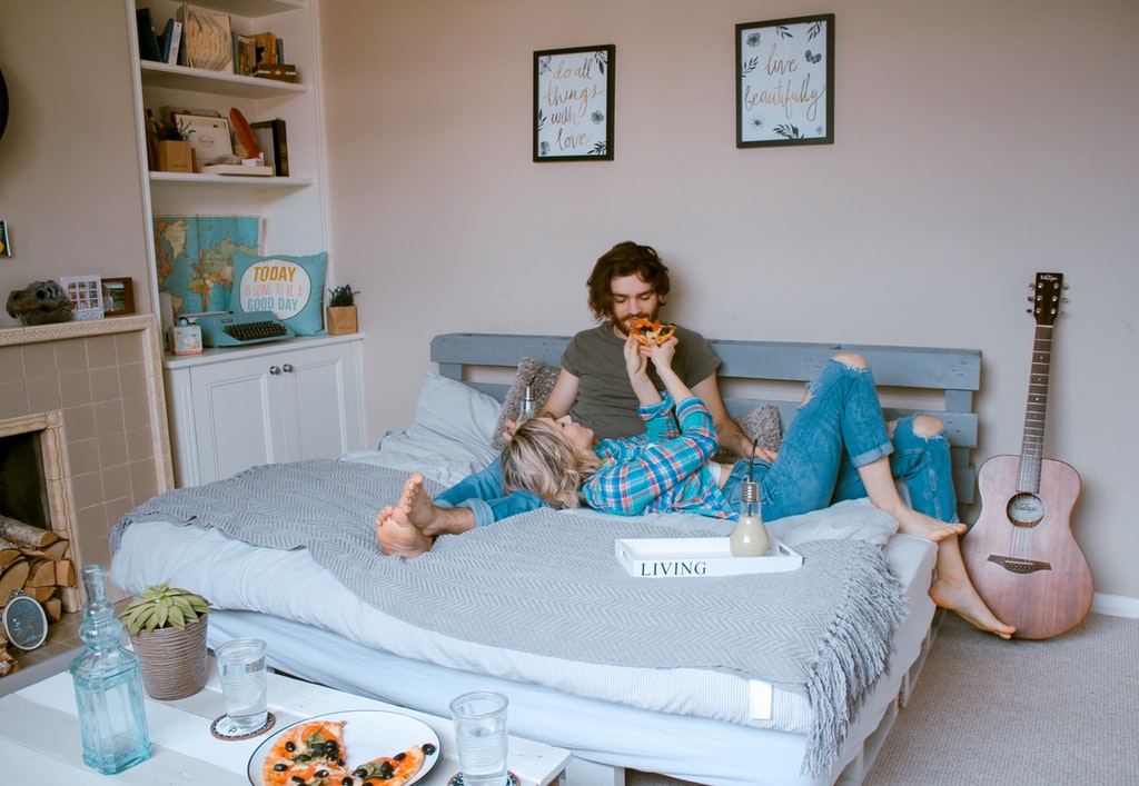 Casal jovem deitado em cama de casal comendo mamão e tomando leite.