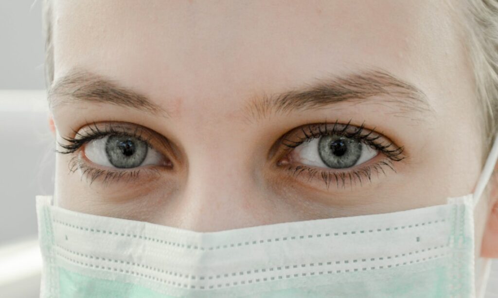 Mulher usando máscara de hospital, apenas seus olhos azuis estão expostos.