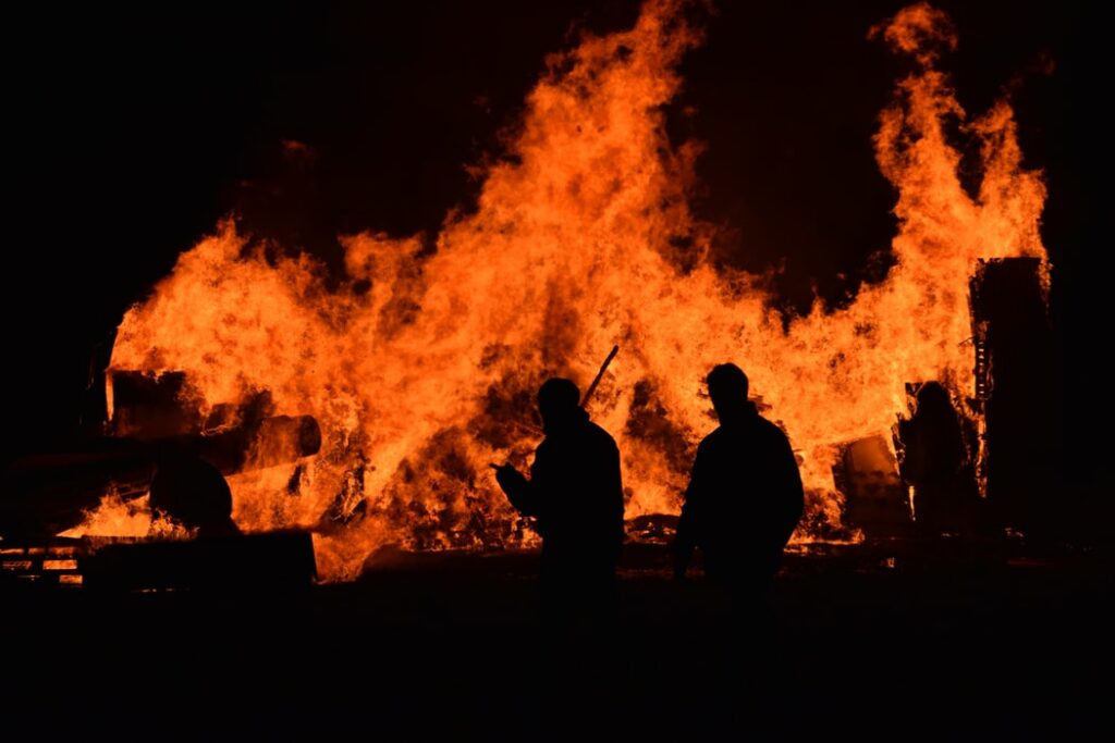 Silhueta de pessoas andando perto de incêndio.