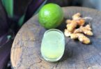 Copo com suco ao lado limão e gengibre sobre uma mesa de madeira.