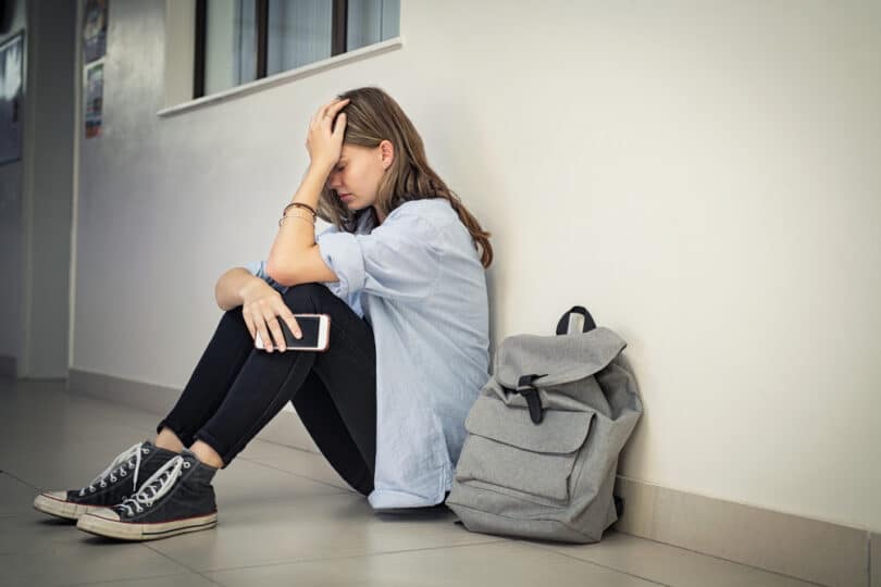 Mulher sentada em um corredor, triste e segurando o celular