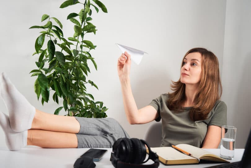Mulher branca em escritório brincando com aviãozinho de papel