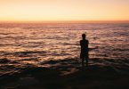 Silhueta de uma pessoa de frente para o mar durante o nascer do sol.