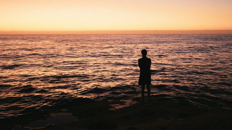 Silhueta de uma pessoa de frente para o mar durante o nascer do sol.