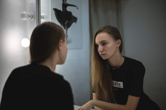 Menina se olhando no espelho com rosto triste