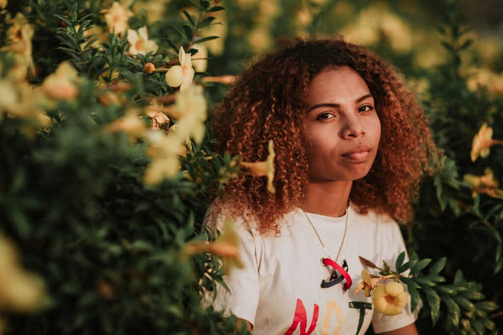 Retrato de mulher de cabelos cacheados em meio a flores amarelas.