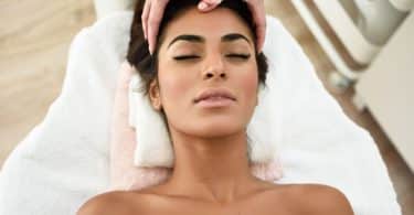 Mulher deitada recebendo massagem na testa.