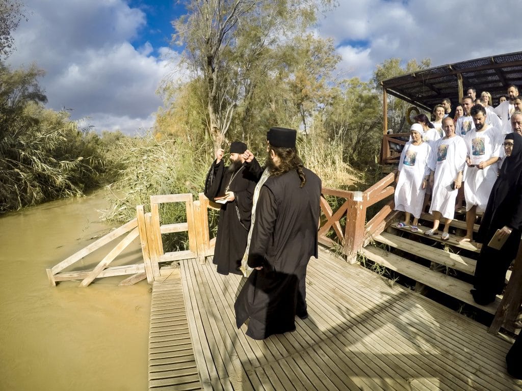Ritual de batismo de pessoas adultas. Os celebrantes vestem túnicas pretas e os batizados túnicas brancas. A cerimônia acontece em um grande rio.