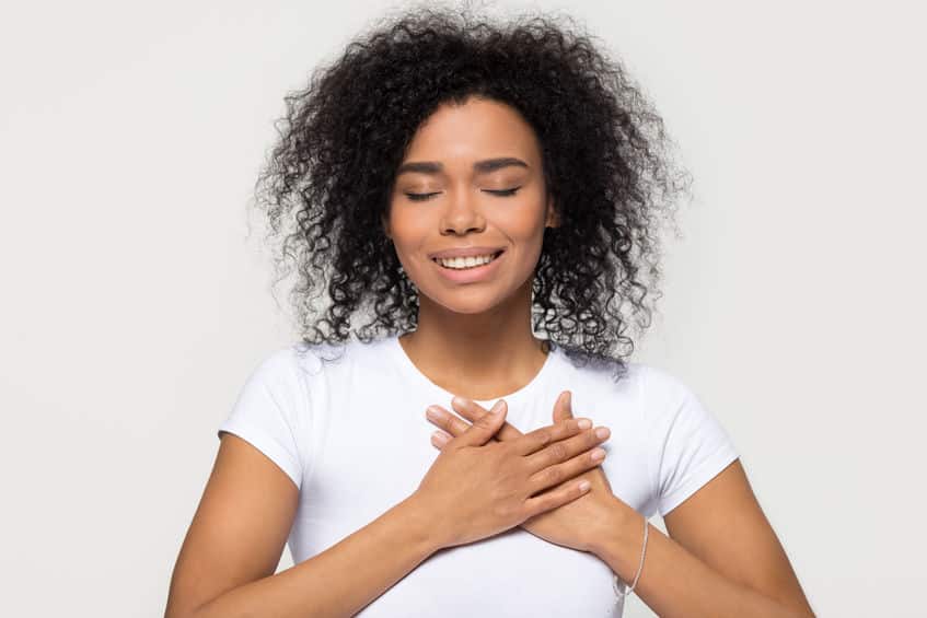 Mulher feliz coloca as mãos sobre o coração, de olhos fechados, em gesto de agradecimento.