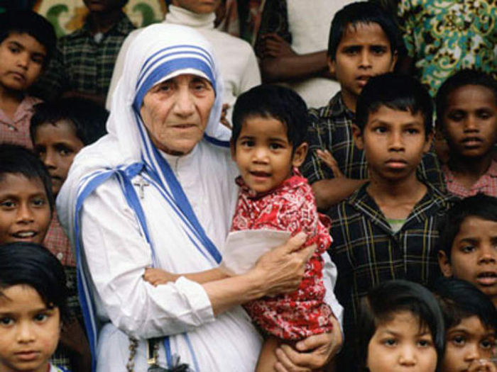 Madre Teresa de Calcutá segurando um menino em seu colo, rodeada por diversos outros meninos.