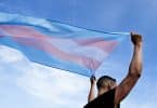 Homem branco segurando bandeira do orgulho transsexual.