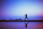 Silhueta de mulher correndo na praia. É possível ver seu reflexo na água.