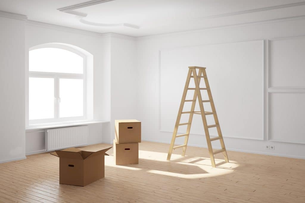 Escada de madeira dentro de uma sala ampla e na cor branca. Ao lado da escada três caixas de papelão. Uma delas está aberta e as outras estão fechadas.