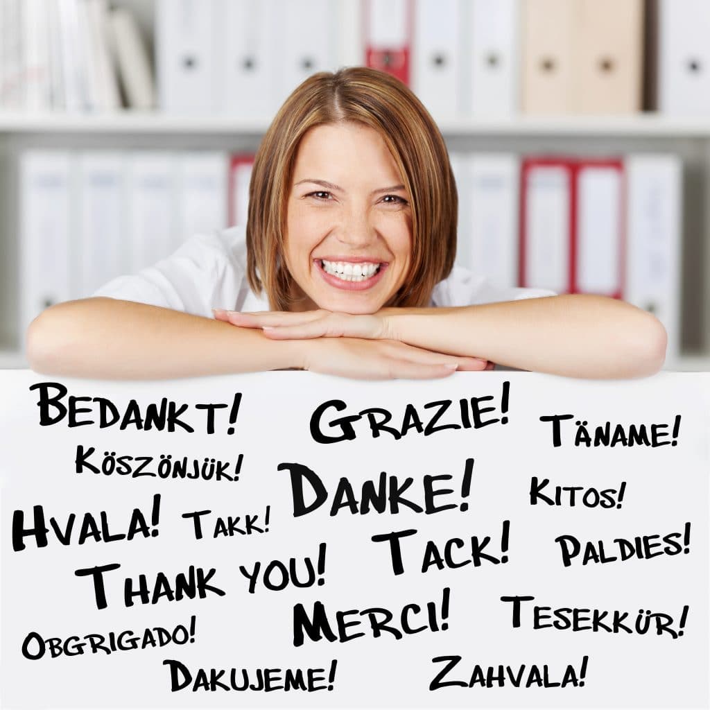 Palavra gratidão escrita em diversos idiomas. Atrás das palavras um mulher feliz e sorridente, sendo grata por tudo que aconteceu em sua vida.