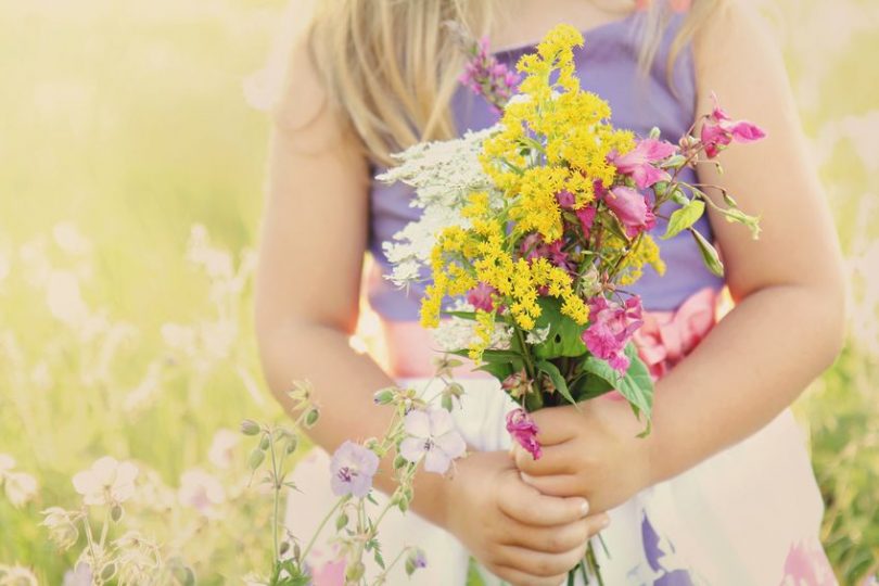 Menina usando vestido segurando um buque de flores em uma campina. A foto corta sua cabeça, vemos apenas seu corpo.