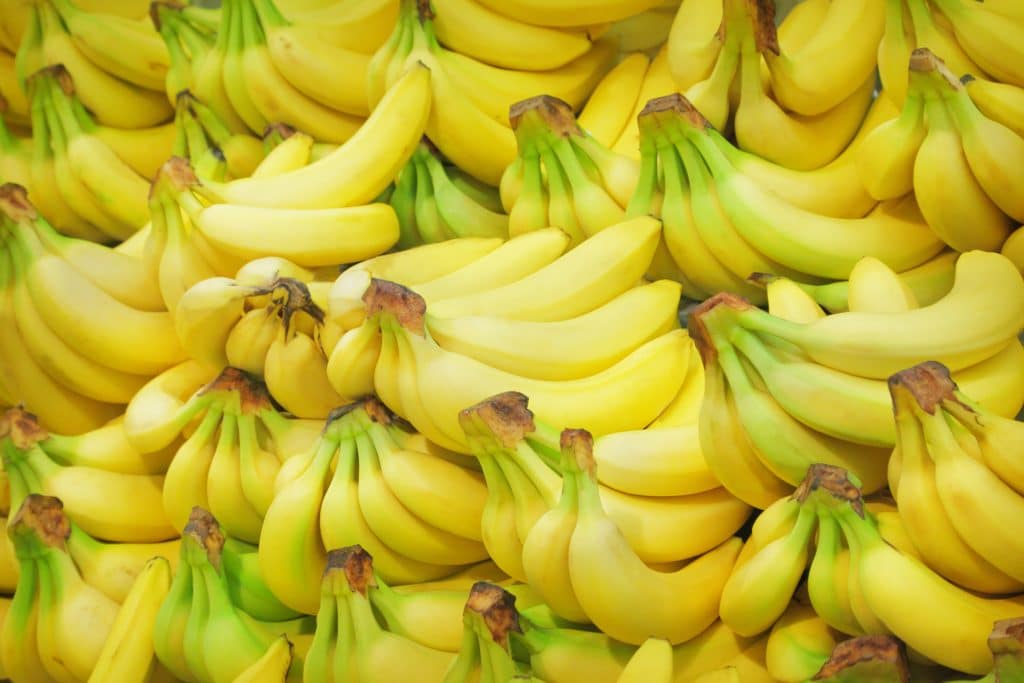 Pilhas de cachos de bananas amarelinhas disponíveis em uma bancada de supermercado.
