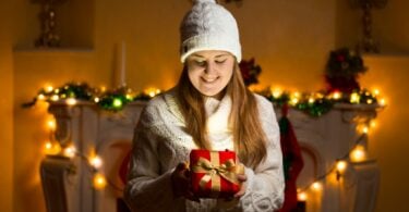 Mulher segurando presente de natal em casa enfeitada com luzes