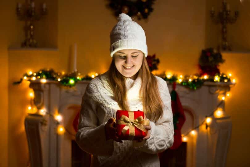 Mulher segurando presente de natal em casa enfeitada com luzes