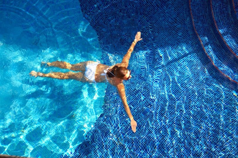 Mulher de biquíni branco nadando na piscina.
