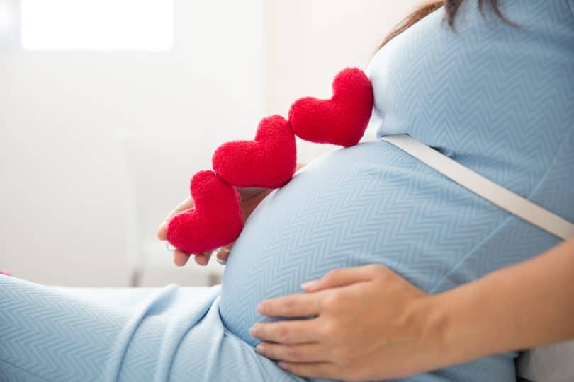 Mulher branca grávida com corações de feltro em cima de sua barriga.