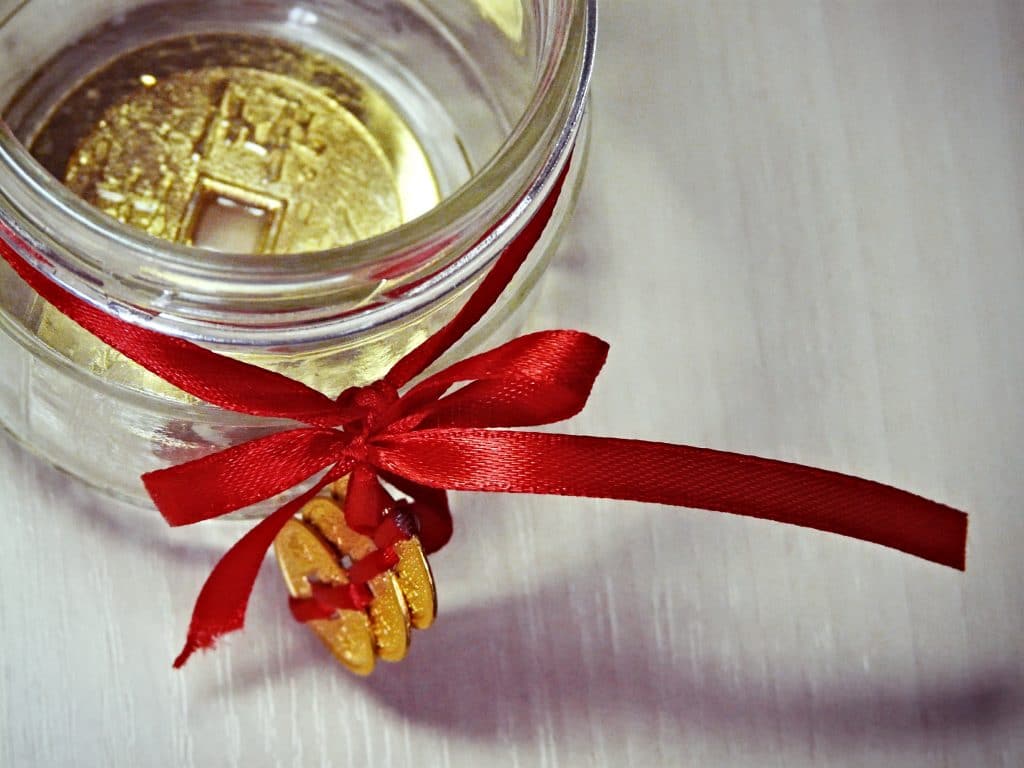 Talismã feito de moeda para Feng Shui. A moeda está armazenada em um recipiente de vidro decorado com um laço de fita vermelho com três moedas douradas penduradas.