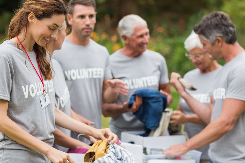 Grupo com seis voluntários usando camisetas cinzas iguais separa roupas em caixas.