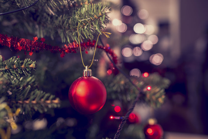 Árvore de Natal decorada com fitas, luzes e enfeites. A foto está bem perto focando em uma bolinha vermelha.