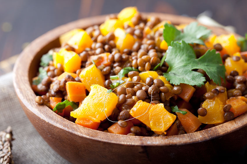 Salada de lentilha com legumes em uma tigela de madeira.