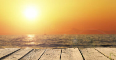 Imagem do mar com um sol forte e laranja no horizonte.