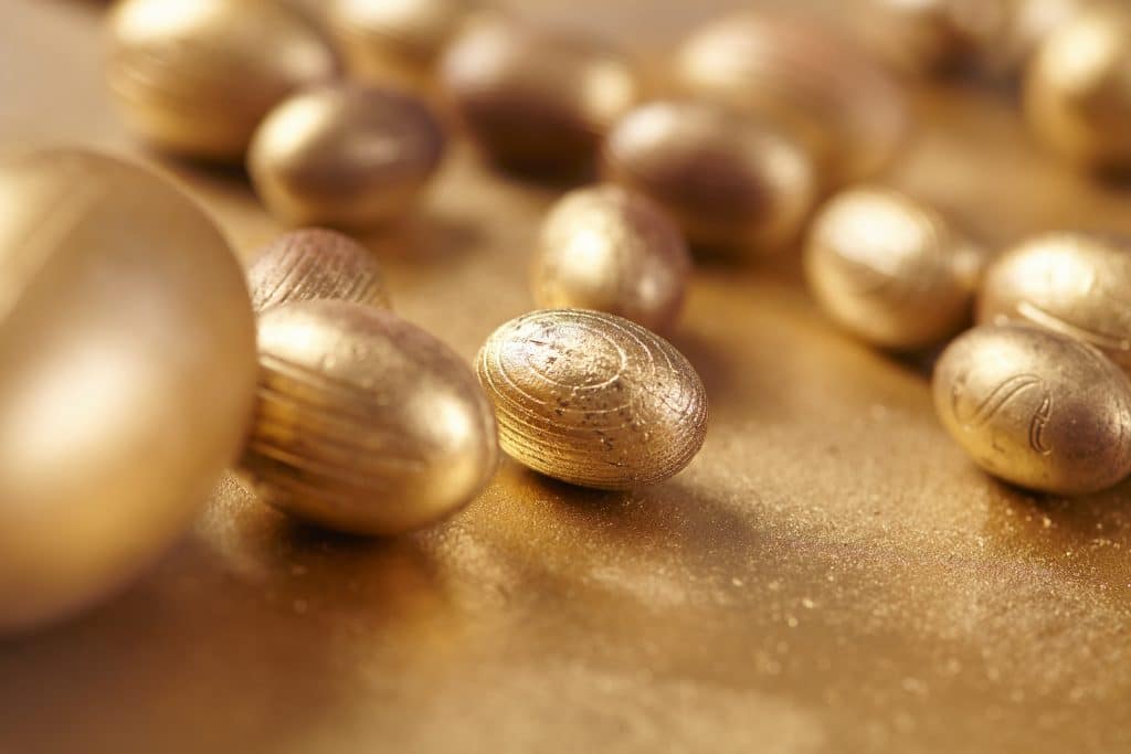 Vários ovos de páscoa de chocolate na cor dourada. Todos estão dispostos sobre uma mesa também dourada.