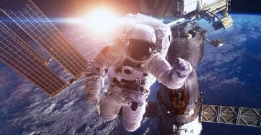 Imagem manipulada de astronauta no espaço, entre um satélite e a Estação Espacial Internacional. Ao fundo, é possível ver o planeta Terra bem perto, e atrás dele, o sol brilhando.