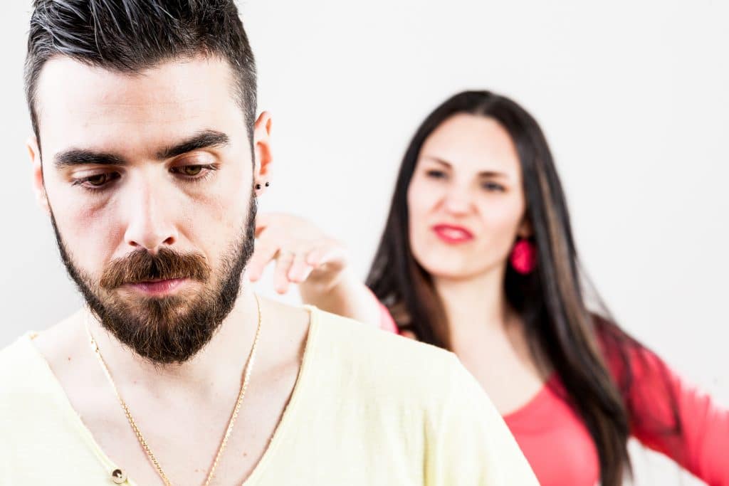 Mulher desprezando o seu esposo. Ela está por trás dele fazendo caretas. Ele está triste.