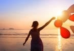 Silhueta de uma mulher na praia, ao pôr do sol, correndo com balões em frente ao mar.
