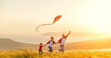 Família correndo em campo com pipa na mão e sol ao fundo