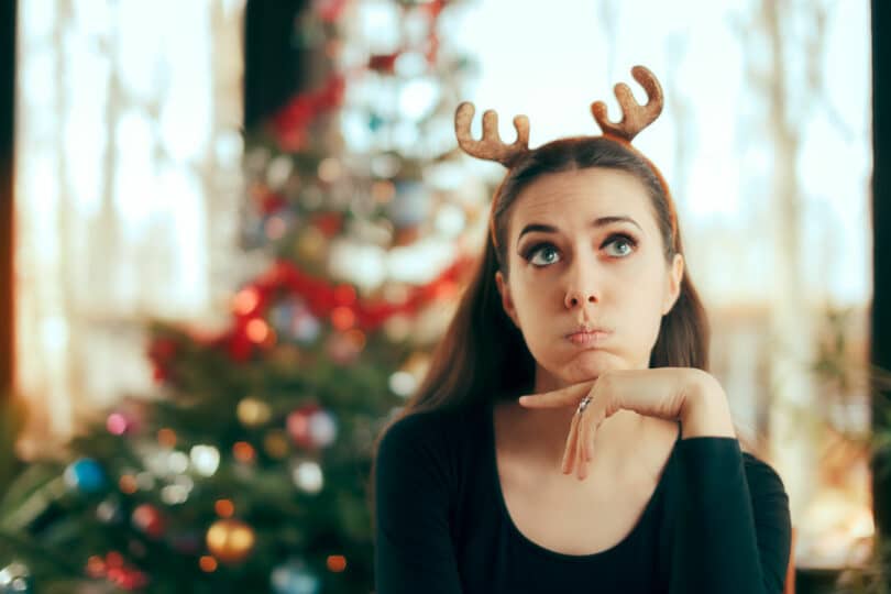 Mulher com arquinho de renas com expressão irritada e árvore de natal ao fundo