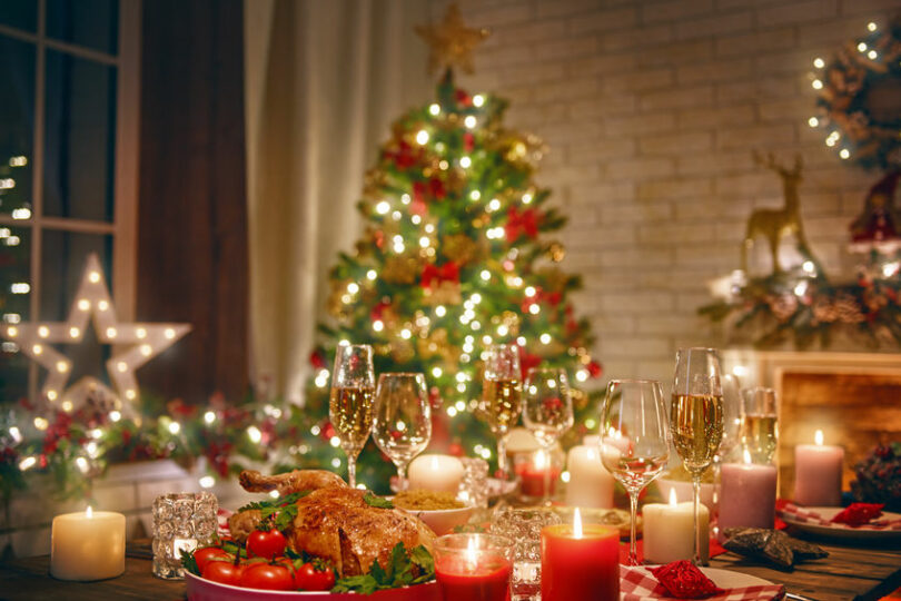 Árvore de Natal decorada ao fundo, e mesa com comida e bebidas para a ceia natalina.