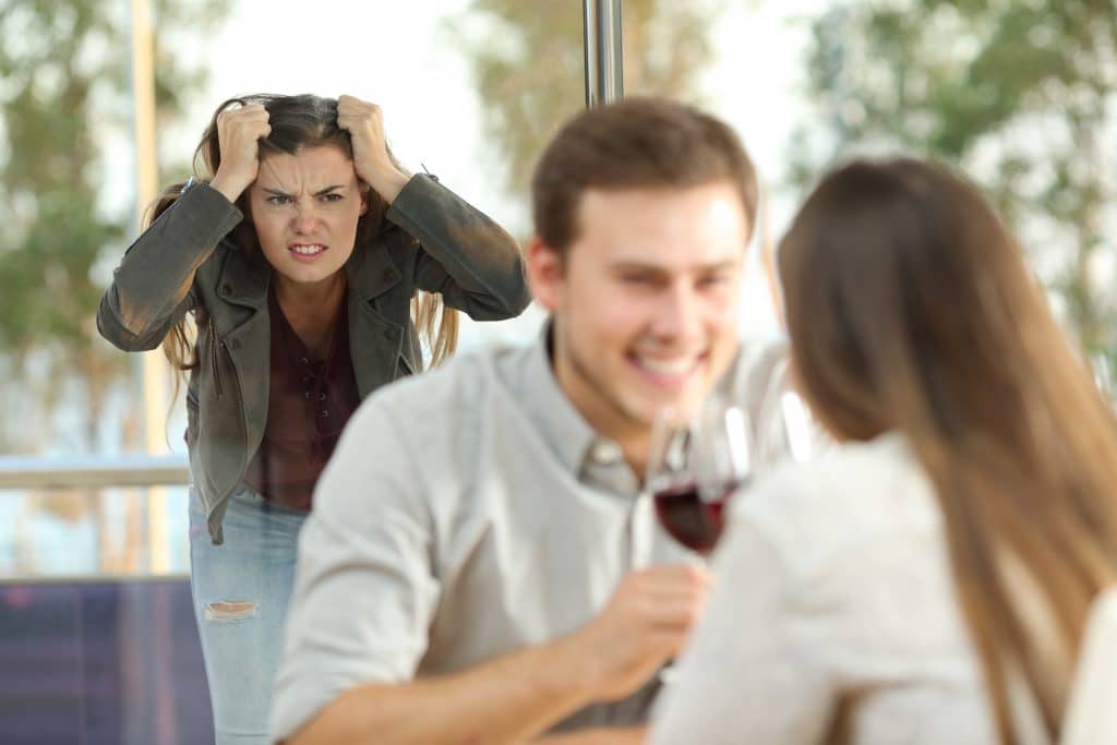 Casal de homem e mulher flertando em um restaurante. Eles estão tomando uma taça de vinho tinto. Ao fundo uma outra mulher preocupada e nervosa olhando para eles. Ela está com as mãos sobre a cabeça. Parece que descobriu a traição do esposo.