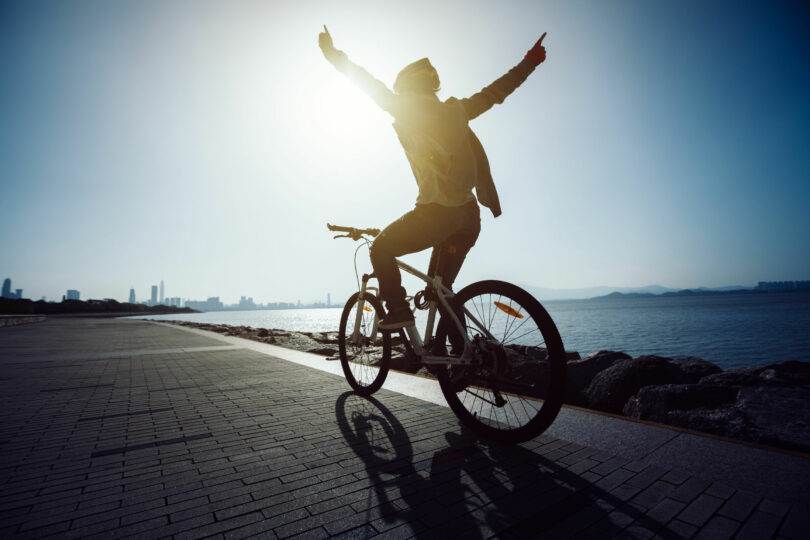 Homem andando de bicicleta com braços para o alto