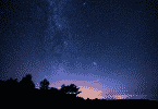 Imagem de um céu de noite, estrelado. Árvores ao fundo.