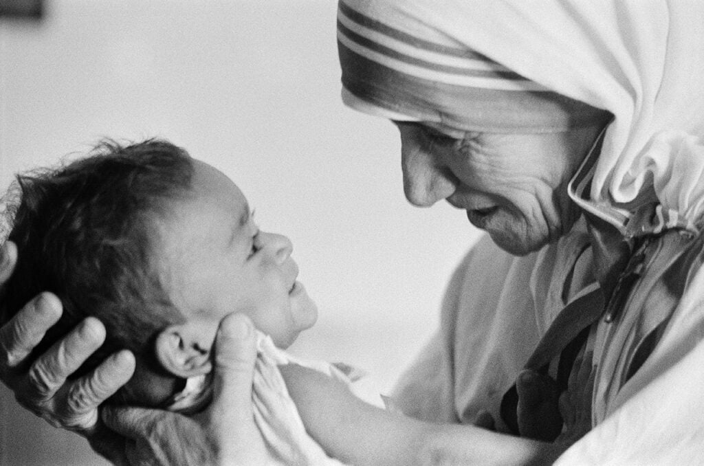 Madre Teresa segurando um bebê bem próximo de si, e olhando para seu rosto.